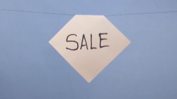 A man hangs a white sheet of paper with a black inscription "sale" on a blue background — Stock Video