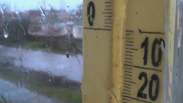 Météo pluvieuse dehors. Gouttes sur le verre de la fenêtre, échelle du thermomètre brumeux — Video