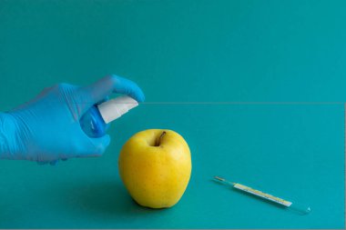 Tarafsız bir arkaplanda termometre ve antiseptik, eldivenli eller, kadın elleri, mavi tıbbi eldivenler, antiseptik tedavi, sarı büyük elma. Grip virüsü veya koronavirüsün tedavisi kavramı.