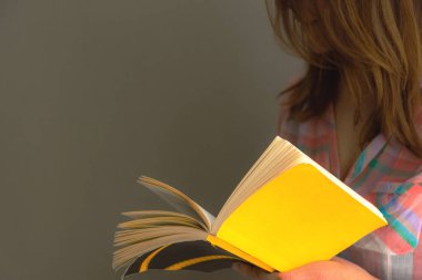 Güzel bir kızın açık bir kitaba bakıp okuduğu resim. Bir kızın elinde açık bir kitap, Kitap Günü. Ev tatili. Evin kendi kendini izole etmesi. Evde olmak güzel..