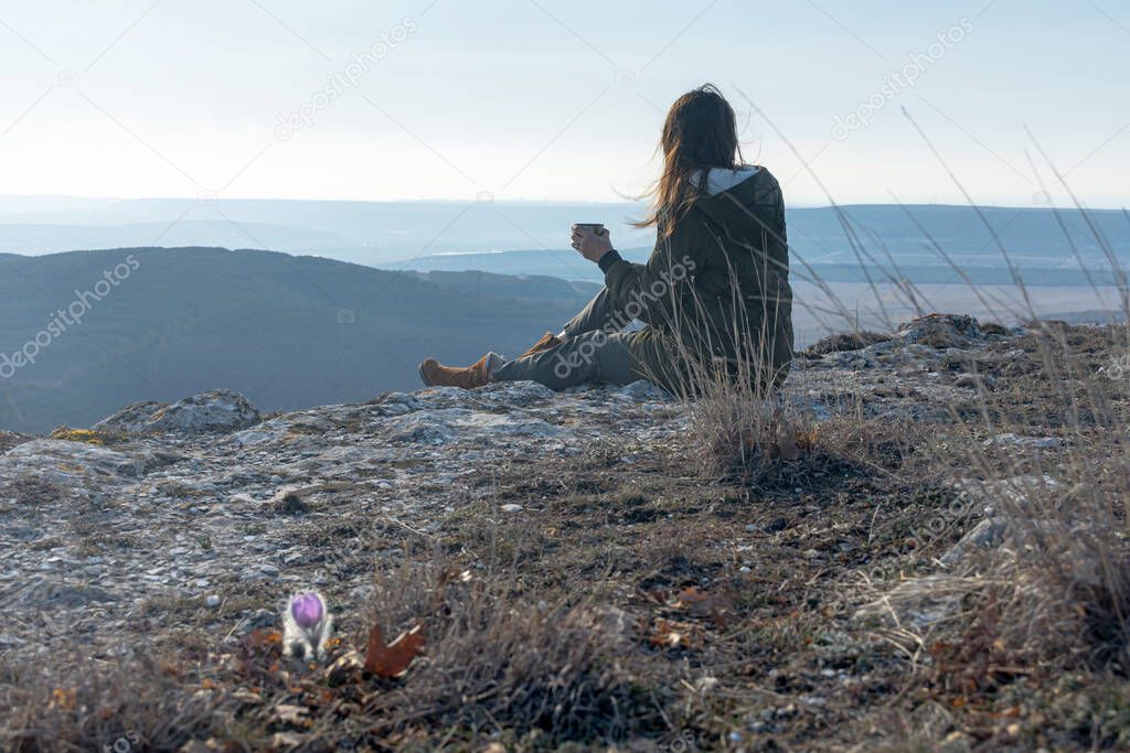 A female traveler drinks tea with a view of the mountain landscape. A girl drinks tea on a cliff in the Crimea. Relax with a beautiful view of the blue distance.