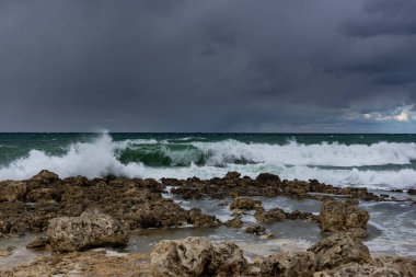 Denizde şiddetli bir fırtına. Güzel mavi fırtına bulutları. Bulutlu, tehditkar bir manzara. Korkunç bir fırtına uyarısı. Dalgalar kayalık sahilde kırılır.