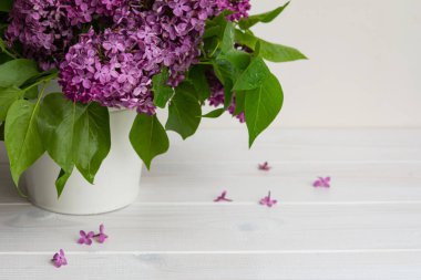 Beyaz arka planda, vazodaki leylak rengi. Ahşap bir masada parlak bir demet leylak. Bahar arka planda. Seçici odak noktasında leylak dalları. Beyaz kovada eski bir buket.