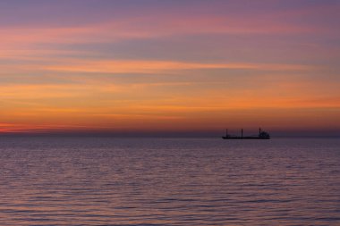 Parlak alacakaranlık gün batımı gökyüzü denizin üzerinde. Güneş battıktan sonra turuncu gözlüklerle harika bir gökyüzü. Doğal arka plan. Deniz ve gökyüzünün mor tonu. Ateş bulutlarının soyut çizgileri. Ufukta bir gemi.