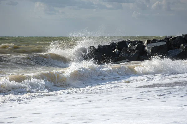 Big waves roll up on the beach. Bright Sunny day and sea surf. White foaming waves and splashes. Beach during a storm. A hot summer day and a stormy sea. High wave. Cloudy seascape.