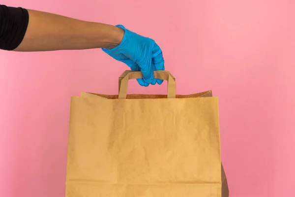 Courier delivery of products in a paper bag. A delivery girl holds a package on a pink background. Delivery by self-isolation. A volunteer delivers food. The concept of food delivery. Take-away food.