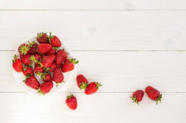 Beyaz ahşap arka plan manzaralı çilek. Beyaz bir tabakta kırmızı çilekler ve masaya saçılmış. Sevdiğim güzel, sakin bir hayat. yaz hala hayattadır. Sağlıklı beslenme kavramı