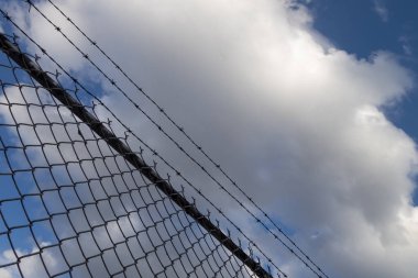 Mavi gökyüzü ve beyaz bulutlu dikenli tel örgü örgü.