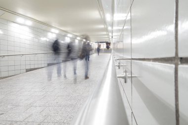 Hareket halindeki insanlar metroya giden parlak beyaz fayanslı tünel geçidinde yürüyorlar. 