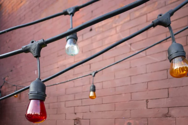 Exterior big hanging bulbs on stinged think rubber wires for decoration near brick walls