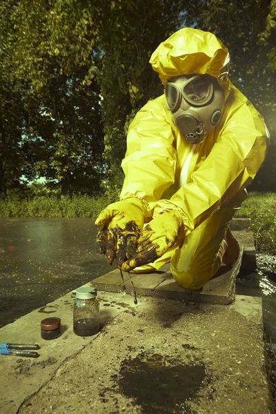 Scientist in yellow protective suit collecting samples of water contamination