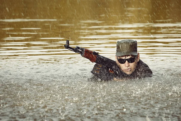 Солдат в форме плавает в озере с автоматом — стоковое фото
