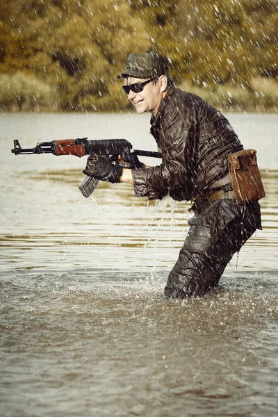Soldier in uniform attacking from lake with assault rifle — Stock Photo, Image