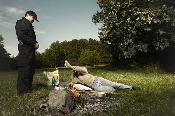 Young vagabond man catched in park by police man by illegal fireplace — Stock Photo, Image