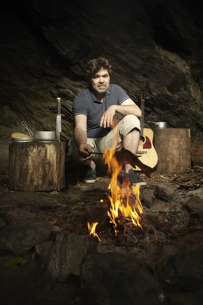 Man relaxing and preparing hunted trout on open fire in wilderness — Stock Photo, Image