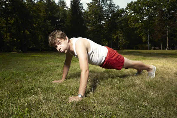 Глупый слабый человек в стиле ретро делает упражнения в парке — стоковое фото