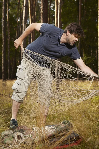 Man in wild forest hanging hammock bed with mate and sleeping bag — Stock Photo, Image