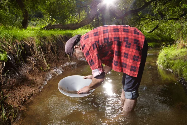 Moderner Goldsucher im Hipster-Stil schwenkt Sand im Bach nach Gold — Stockfoto