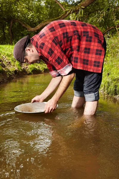 Moderner Goldsucher im Hipster-Stil schwenkt Sand im Bach nach Gold — Stockfoto