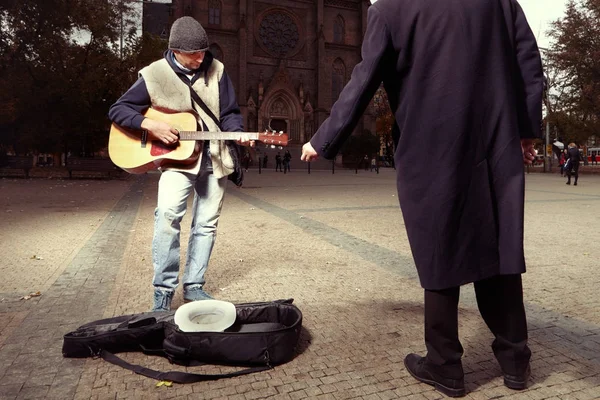 Unknown man stealing money to beggar with guitar — Stock Photo, Image