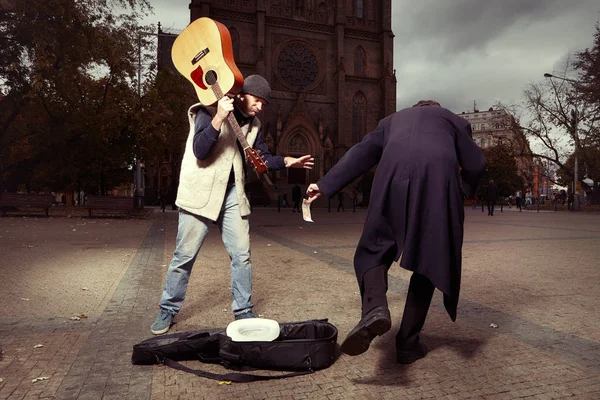 Homem desconhecido roubando dinheiro para mendigo com guitarra — Fotografia de Stock