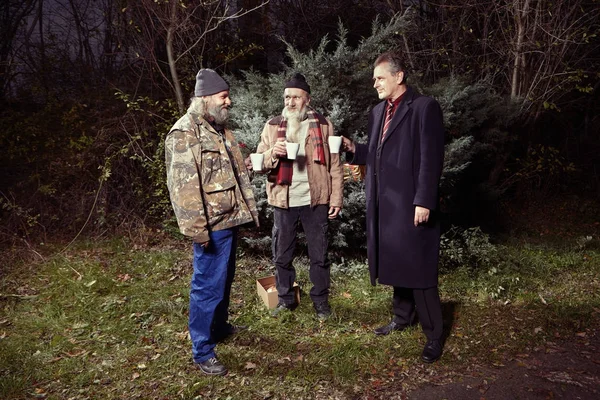 Man in suit met two homeless men in winter park — Stock Photo, Image