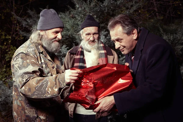 Man in suit get a christmas gift from two homeless men — Stock Photo, Image