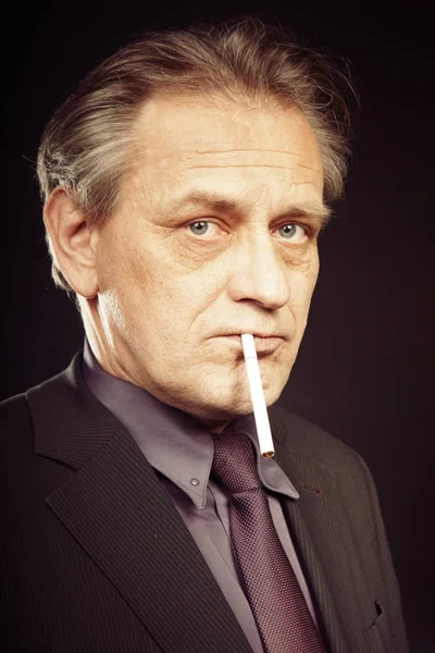 Older caucasian man smoking classic cigarette on black background