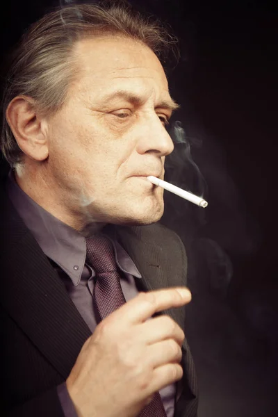 Older caucasian man smoking white cigarette on black background