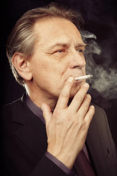 Older caucasian man smoking cigarette on black background