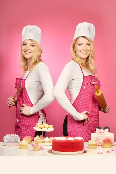 Nice blonde twins baking cakes posing with their sweets by table