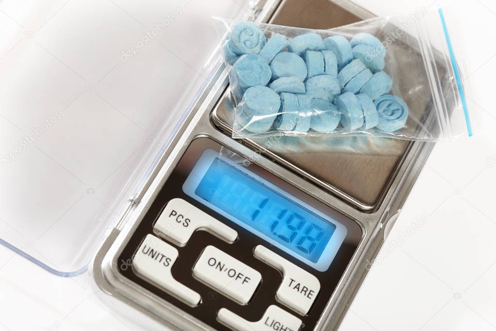 Pills of MDMA synthetic drugs on small digital scale