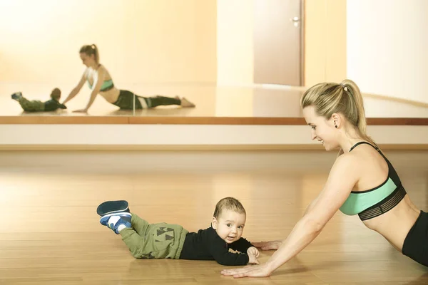 Mirroring young fitness woman exercising with her infant son