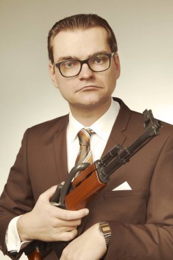 Takım elbiseli adam otomatik silahla poz veriyor.