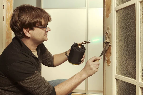 家の男はバーナー付きドアから古い塗料の重い層を削除します — ストック写真