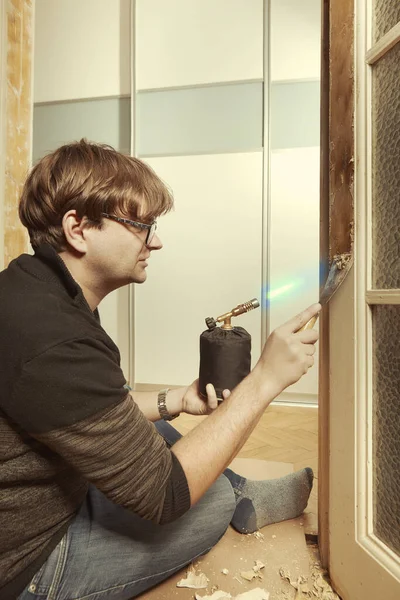 Man at home removing havy layer of old paint from door with burner