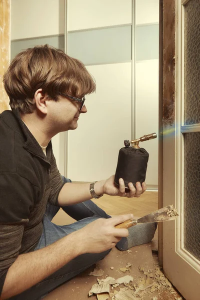 男人在家里用燃烧器从门上取去长春藤色的旧油漆 — 图库照片