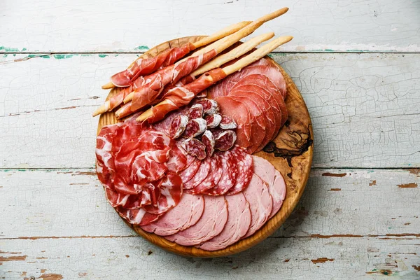 Cold meat plate Italian snacks food with ham, prosciutto, salami, pork chops, sausage and grissini bread sticks on wooden background