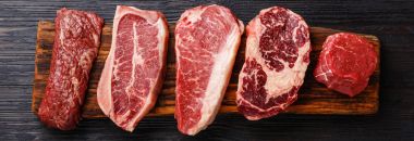 Variety of Raw Black Angus Prime meat steaks Machete, Blade on bone, Strip-loin, Rib eye, Tenderloin fillet on wooden board