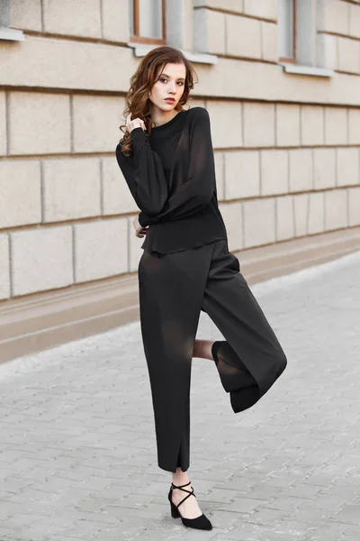 Брюнетка в черной блузке и позах брюк на городской улице в солнечный день — стоковое фото