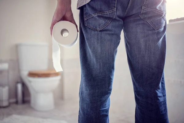 Homem segurando rolo de papel higiênico no banheiro — Fotografia de Stock