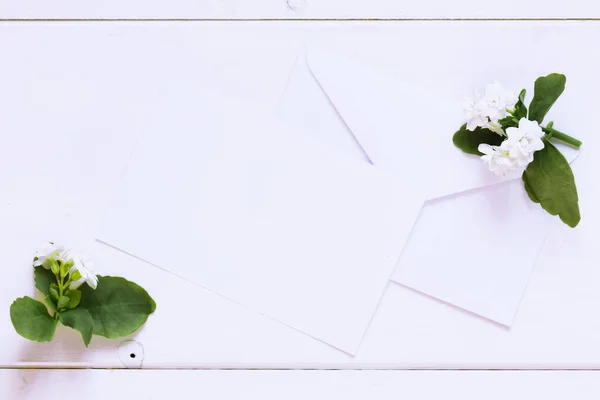 Blank white greeting card with white envelope and white flowers with on a wooden table, Mock up for invitation, space for your spring or romantic text