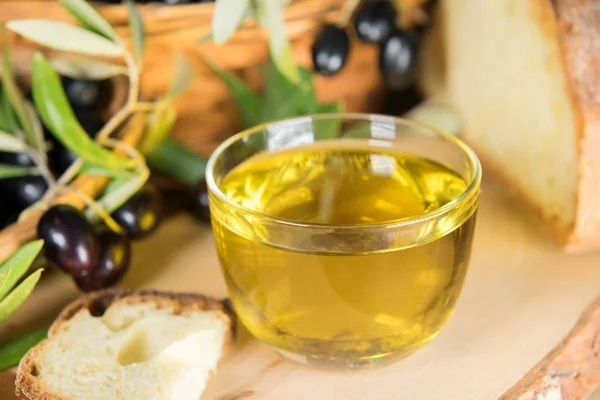 Primer plano de un cuenco de vidrio lleno de aceite de oliva con pan y brunches de oliva. grasas saludables — Foto de Stock