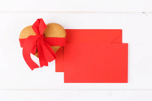 Biscoitos em forma de coração com fita vermelha e cartão de cumprimentos de mockup vermelho em um fundo branco. Símbolo de amor acolhedor e Dia dos Namorados backrgound — Fotografia de Stock