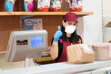 Avetrana, İtalya, Marth 16, 2020. Tıbbi maske ve eldiven takan satıcı kadın her şeyin yoluna gireceğini gösteriyor.