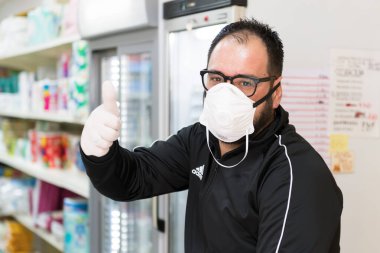 Avetrana, İtalya, Marth 16, 2020. Tıbbi maske ve eldiven takan satıcı her şeyin yoluna gireceğini gösteriyor.