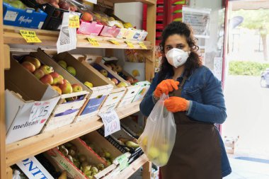 Avetrana, İtalya, Marth 16, 2020. İtalyan bir manav, Coronavirus epidemisi sırasında tıbbi maske ve eldiven takarak bir poşet elma servis ediyor. Alışveriş, Covid-19 pandemisi