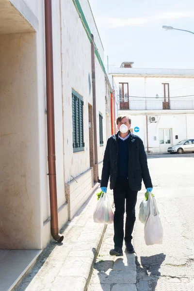 Empty street, a man returns home with purchases from shopping wearing protective face masks and gloves to contain the spread of coronavirus, Italy during quarantine. Respect health standards covid-19