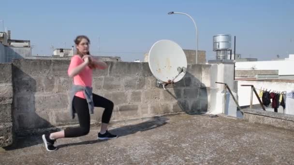 Будинок ізольований. Молода дівчина займається спортом на даху свого будинку під час карантину. Фітнес-тренінги для жінок у спортивному одязі. Концепція спорту та здоров'я. Карантинний спорт вдома — стокове відео