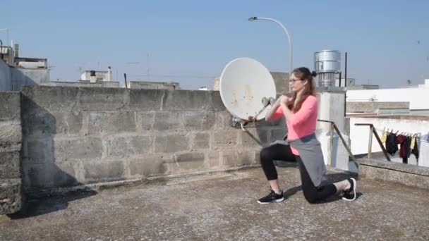 Home isolated. Young girl is doing sports on the roof of her home during quarantine. Female fitness training in sportswear. Concept of sport and health. Quarantine sport at home — Stock Video